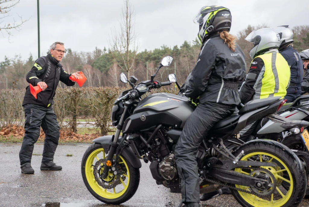 Motorrijinstructeur geeft training met pylonen aan groep motorrijders